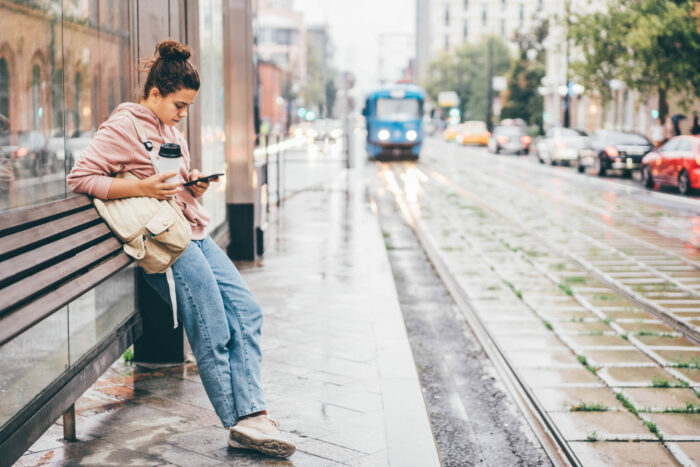 Woman waiting for public transport on bus stop looking at phone