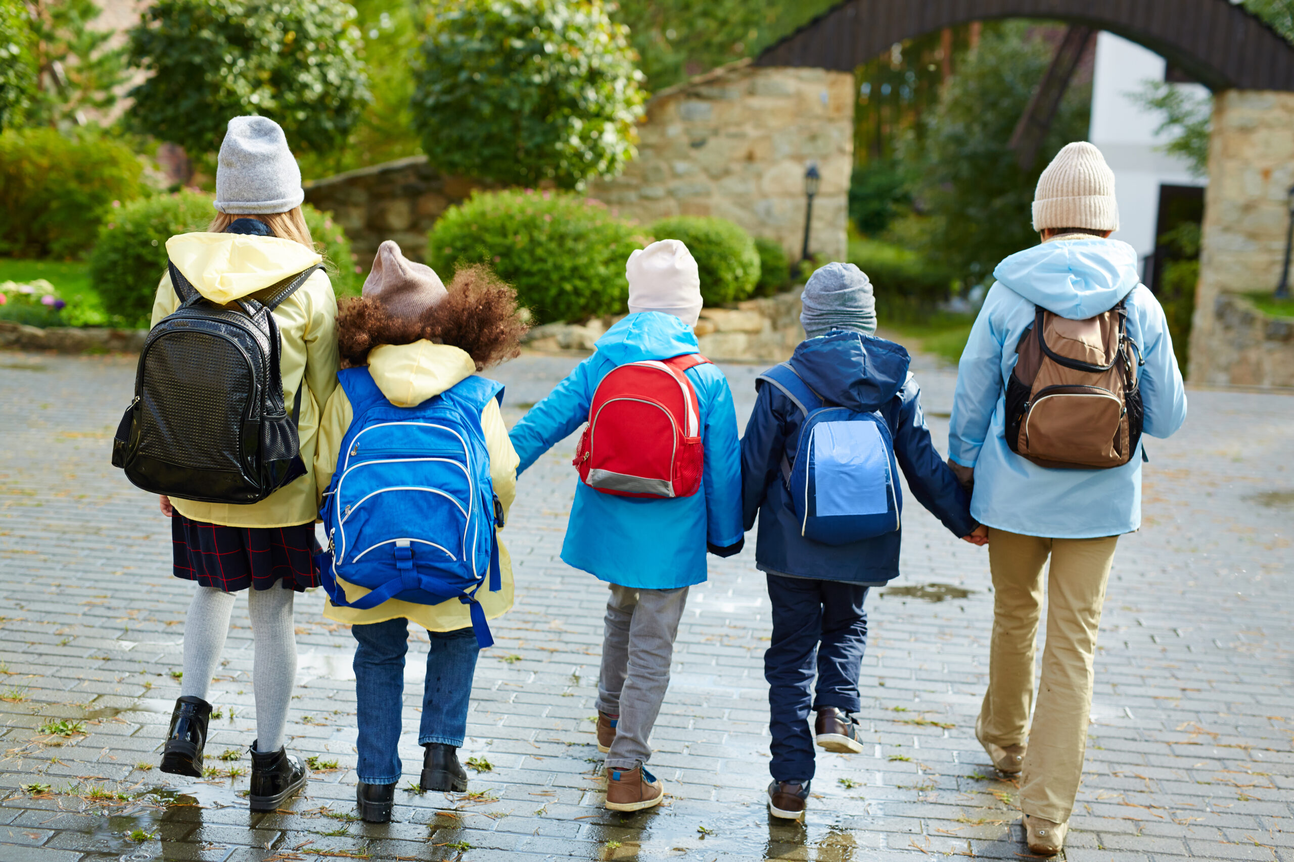 Five schoolkids in casualwear with rucksacks on backs holding by hands while going to school