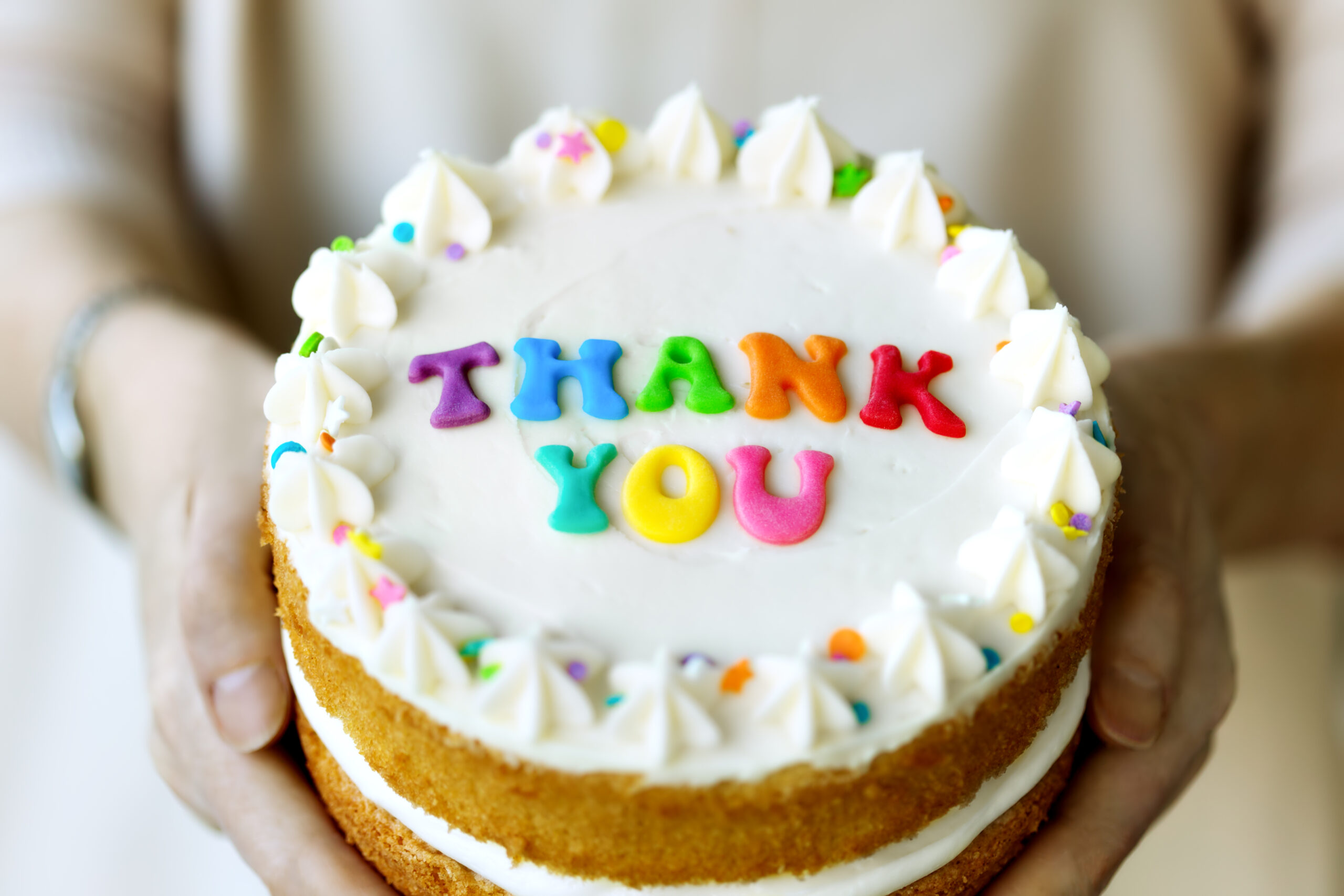 Hands holding cake with colorful rainbow letters spelling thank you