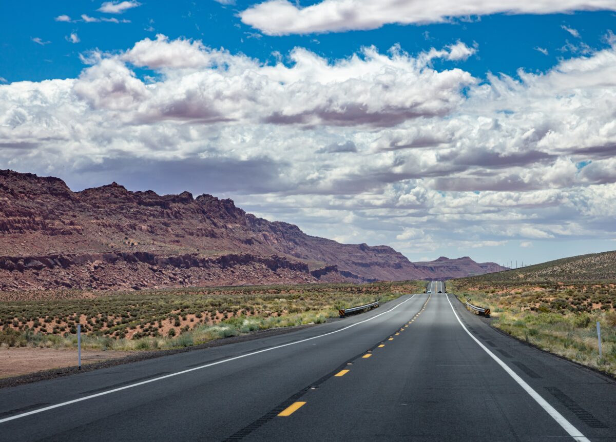 Highway in a sunny spring day, countryside USA. Empty national road, passing through American desert, Blue cloudy sky background