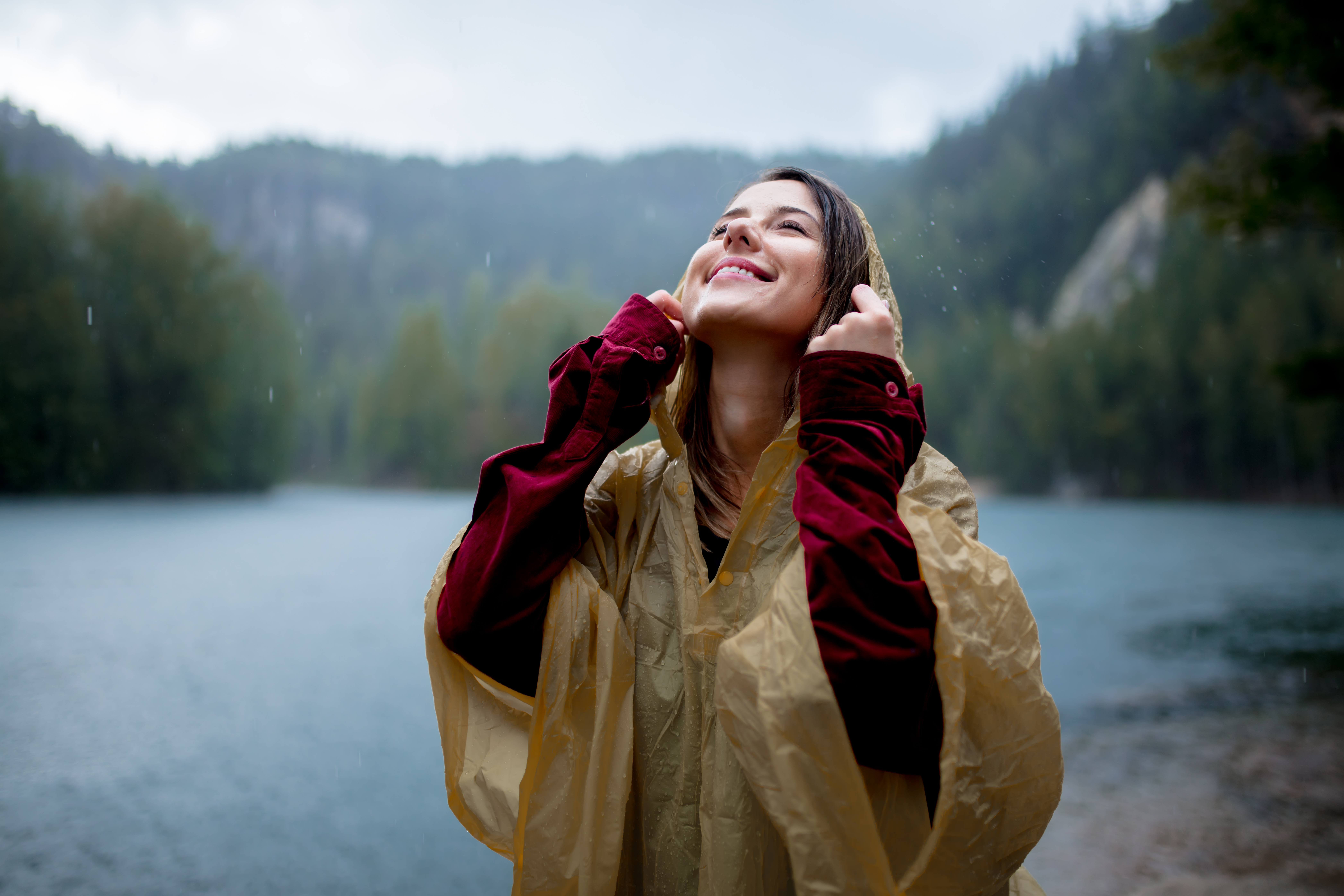 Young woman in raincoat near lake in rainy day.