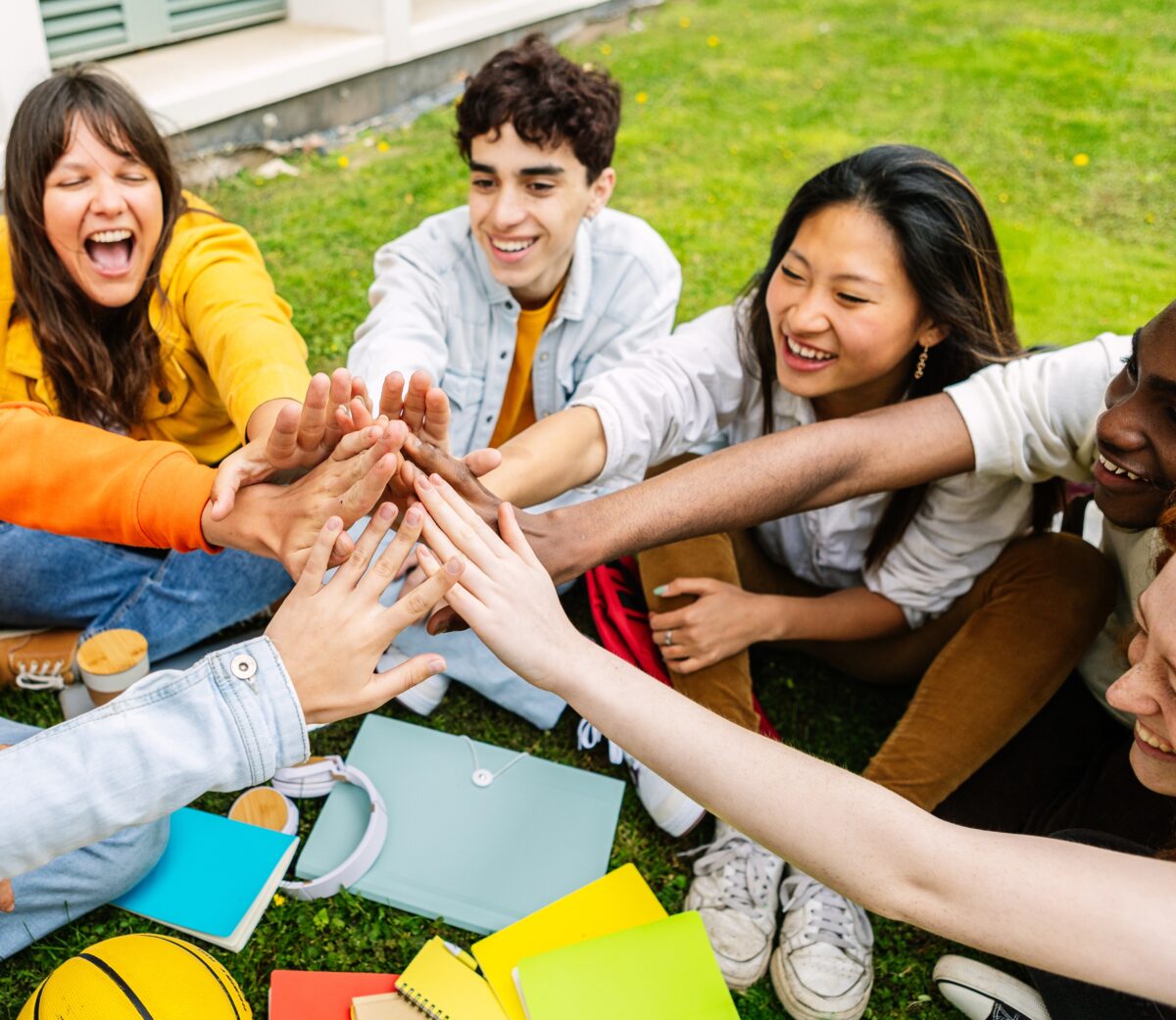 Joyful group of diverse young adults giving high five together outdoors